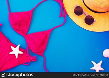 Top view yellow summer hat and bikini, bikini,sunglasses,seashell on vivid blue background.Summer vacation holiday backdrop.copy space for adding text