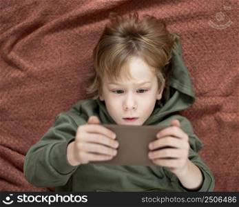 top view young boy using smartphone bed