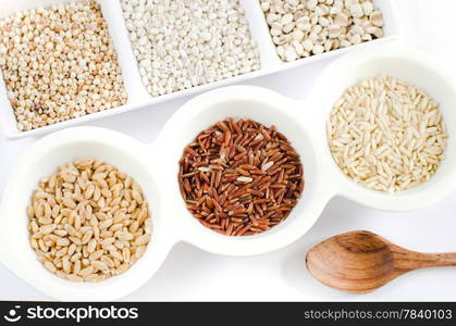 top views of grain and wooden spoon , rice , red rice , wheat, job&rsquo;s tears , barley and millet grains on white bowl