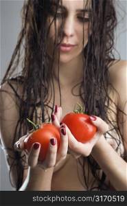 Topless Caucasian woman holding tomatoes.