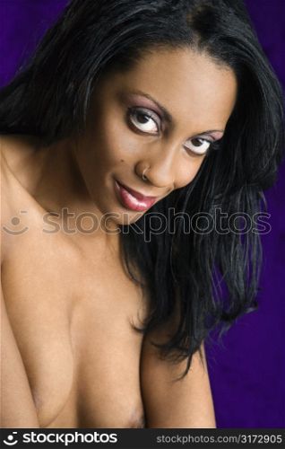 Topless mid-adult African American woman posing on purple background looking at viewer.