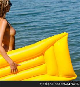 Topless summer woman with yellow mattress by sea water