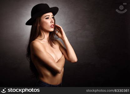 Topless woman wearing blue jeans, panties and hat on black background