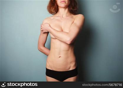 Topless young woman with slender body is wearing black underwear and covering her breasts