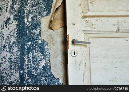 Torn vintage wallpaper peeling paint wall and wooden door in abandoned house.