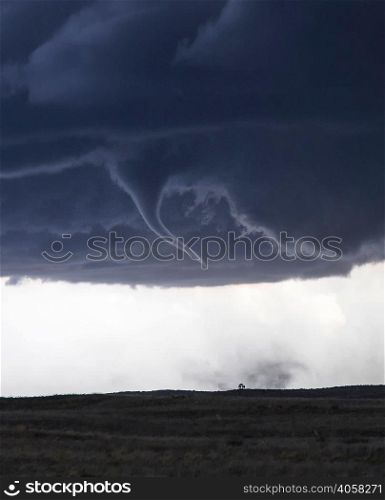 Tornado with funnel cloud over field landscape
