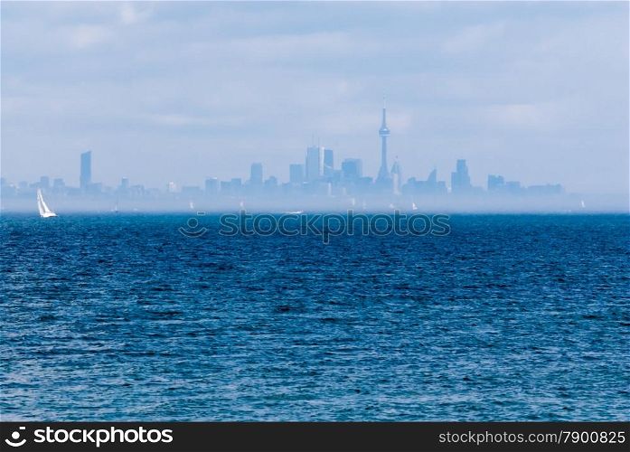 Toronto city skyline across rippled water and fog with sailboat.