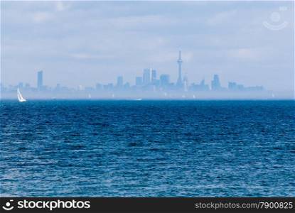 Toronto city skyline across rippled water and fog with sailboat.
