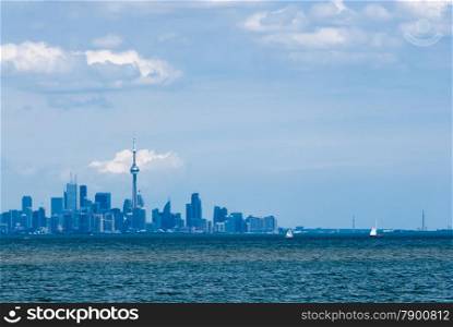 Toronto city skyline from across rippled water against cloudy sky.