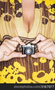 Torso of Caucasian woman holding miniature toy camera.