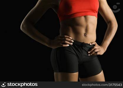 Torso of muscular African American woman wearing athletic apparel with hands on hips.