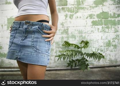 Torso shot of Caucasian mid-adult blonde woman wearing blue jean mini skirt with underwear showing beside building in alley.