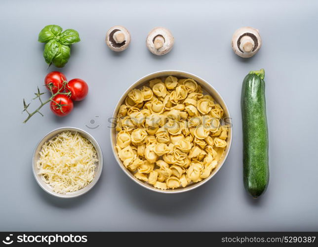 Tortellini bowl with zucchini, mushrooms and vegetarian cooking ingredients on kitchen table background with cutting board , top view, flat lay. Healthy cooking and eating. Italian food concept