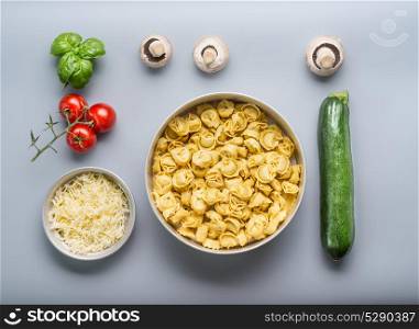 Tortellini bowl with zucchini, mushrooms and vegetarian cooking ingredients on kitchen table background with cutting board , top view, flat lay. Healthy cooking and eating. Italian food concept