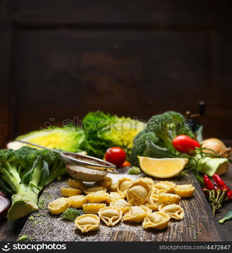 Tortellini Making with vegetales ingredients on rustic kitchen table over dark wooden background. Italian food concept.