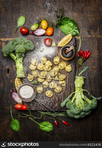 Tortellini with fresh vegetables , preparation with flour on rustic wooden background, top view. Vegetarian food and healthily cooking concept.