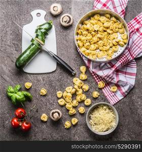 Tortellini with zucchini and vegetarian cooking ingredients on kitchen table background with cutting board and knife, top view. Healthy cooking and eating. Italian food concept