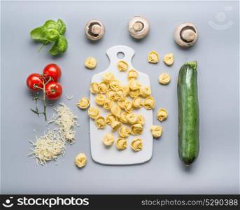 Tortellini with zucchini, mushrooms and vegetarian cooking ingredients on kitchen table background with cutting board , top view, flat lay. Healthy cooking and eating. Italian food concept