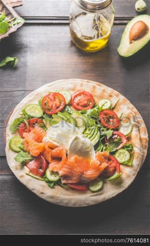 Tortilla with salmon,avocado, cheese, arugula, tomatoes and cucumbers. Flat bread with ingredients on a wooden table. Tortilla wrap preparation. Top view. Close up. Healthy snack or lunch food