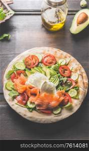 Tortilla with salmon,avocado, cheese, arugula, tomatoes and cucumbers. Flat bread with ingredients on a wooden table. Tortilla wrap preparation. Top view. Close up. Healthy snack or lunch food
