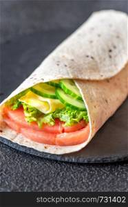 Tortilla wrap with salmon, cheese and vegetables on the stone board