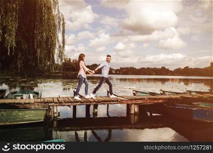 Totally in love. Happy young couple outdoors. young love couple running along a wooden bridge holding hands. love story at the lake. Happy young couple outdoors. young love couple running along a wooden bridge holding hands.