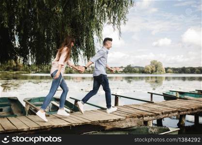 Totally in love. Happy young couple outdoors. young love couple running along a wooden bridge holding hands. love story at the lake. Happy young couple outdoors. young love couple running along a wooden bridge holding hands.