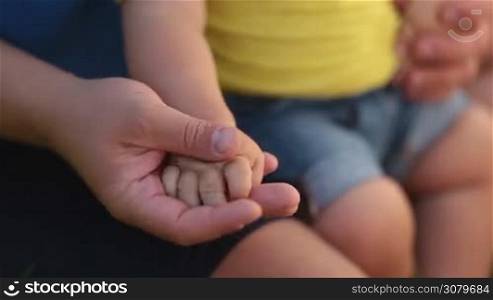 Touch of love. Loving father caressing toddler son&acute;s tiny hand in his palm. Closeup. Small infant baby boy holding parent&acute;s hand and clapping. Concept of love, support, tenderness, care and bonding.