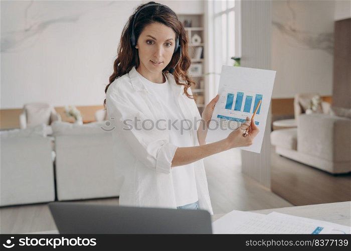Tough spanish woman has corporate internet session on laptop. Young pretty leader shows charts and pointing to the data. Businesswoman is brainstorming online from home. Remote business on quarantine.. Woman has corporate internet session. Young pretty leader shows charts and pointing to the data.