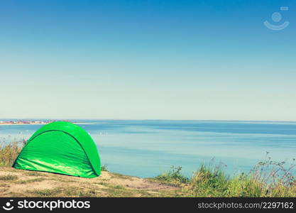 Tourism and recreation. Small green tent in natural area surrounded by meadow water sea lake.. Tourist tent in nature area.