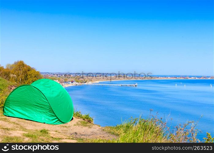 Tourism and recreation. Small green tent in natural area surrounded by meadow water sea lake.. Tourist tent in nature area.