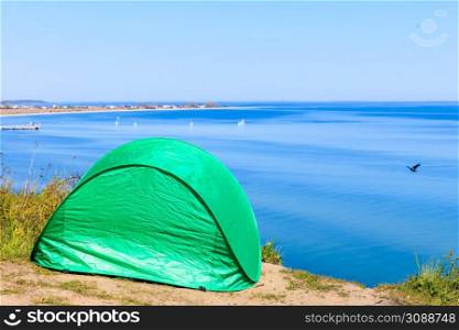 Tourism and recreation. Small green tent in natural area surrounded by meadow water sea lake.. Tourist tent in nature area.