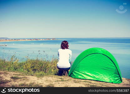 Tourism and recreation. Small green tent in natural area surrounded by meadow water sea lake. Woman spending time on fresh air.. Woman and tourist tent in nature area.