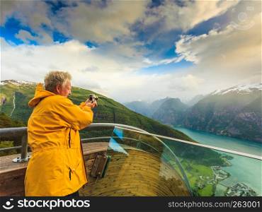 Tourism and travel. Male tourist nature photographer taking photo with camera, enjoying Aurland fjord landscape from Stegastein lookout, Norway Scandinavia.. Tourist photographer with camera on Stegastein lookout, Norway