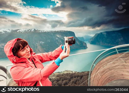 Tourism and travel. Woman tourist nature photographer taking photo with camera, enjoying Aurland fjord landscape from Stegastein lookout, Norway Scandinavia.. Tourist photographer with camera on Stegastein lookout, Norway