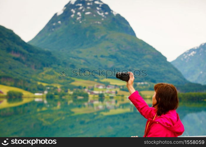 Tourism and travel. Woman tourist taking photo with camera, enjoying fjord mountains view, Sogn og Fjordane county. Norway Scandinavia.. Tourist taking photo at norwegian fjord lake