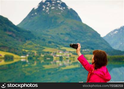 Tourism and travel. Woman tourist taking photo with camera, enjoying fjord mountains view, Sogn og Fjordane county. Norway Scandinavia.. Tourist taking photo at norwegian fjord lake