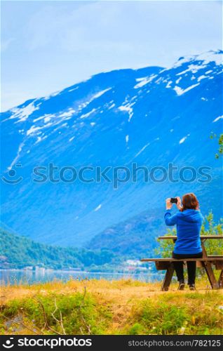 Tourism and travel. Woman tourist taking photo with camera, enjoying mountains lake Oppstrynsvatnet view in Jostedalsbreen National Park, Oppstryn (Stryn), Sogn og Fjordane county. Norway Scandinavia.. Tourist taking photo at norwegian fjord