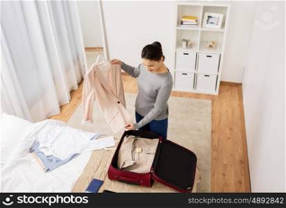tourism, business trip, people and luggage concept - happy young woman packing travel bag at home or hotel room