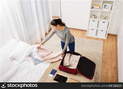 tourism, business trip, people and luggage concept - happy young woman packing travel bag at home or hotel room. woman packing travel bag at home or hotel room