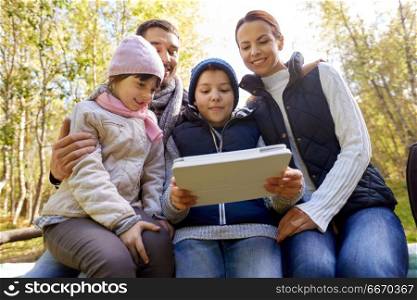 tourism, family and technology concept - happy mother, father, son and daughter sitting on bench with tablet pc computer at camp in woods. family sitting on bench with tablet pc at camp. family sitting on bench with tablet pc at camp