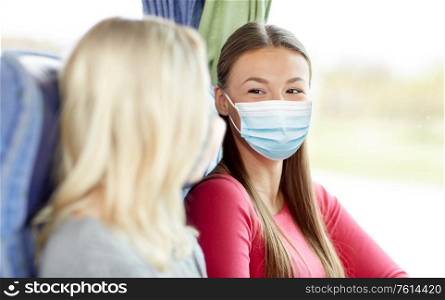 tourism, healthcare and pandemic concept - young women wearing face protective medical mask for protection from virus disease sitting and talking in travel bus. young women in masks sitting in travel bus