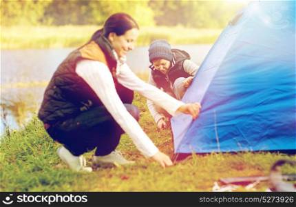 tourism, hike and family concept - happy mother and son setting up tent outdoors. happy mother and son setting up tent outdoors