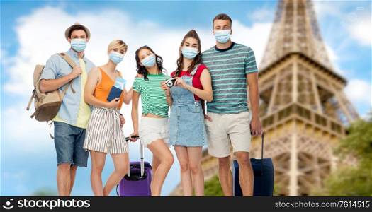 tourism, pandemic and health care concept - group of friends wearing face protective mask for protection from virus disease with travel bags, air tickets and camera over eiffel tower background. friends in masks with travel bags at eiffel tower