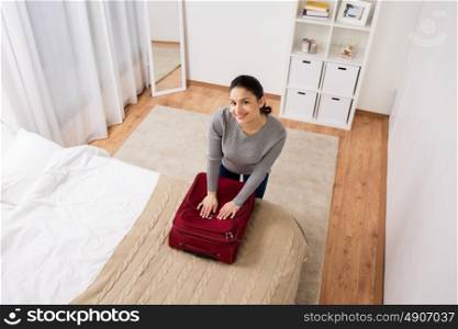 tourism, people and luggage concept - happy young woman packing travel bag at home or hotel room. woman packing travel bag at home or hotel room