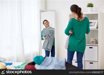 tourism, people and luggage concept - happy young woman packing travel bag at home or hotel room and looking to mirror. woman packing travel bag at home or hotel room