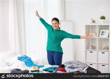 tourism, people and luggage concept - happy young woman packing travel bag at home or hotel room. happy woman packing travel bag at home