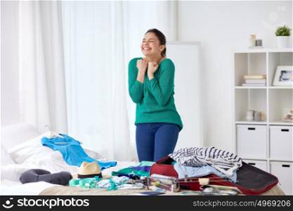 tourism, people and luggage concept - happy young woman packing travel bag at home or hotel room. happy woman packing travel bag at home
