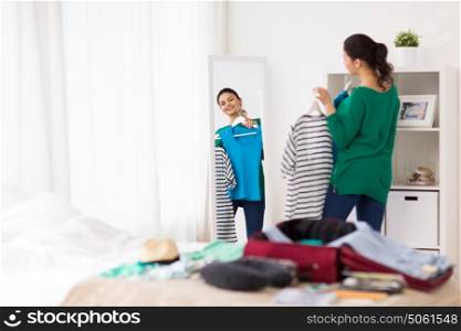 tourism, people and luggage concept - happy young woman packing travel bag at home or hotel room and looking to mirror. woman packing travel bag at home or hotel room