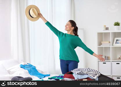 tourism, people and luggage concept - happy young woman with hat packing travel bag at home or hotel room. woman packing travel bag at home or hotel room